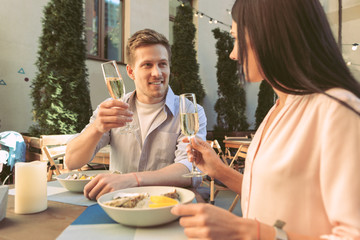 Joyful good-looking couple drinking sparkling wine in tall glasses