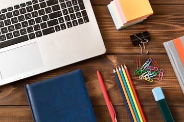 Laptop, notebook, pen, pencils on wooden table. Various office supplies on wooden background.