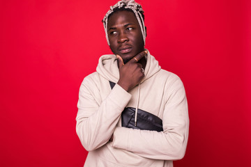 Handsome african man with shaved head, folded arms and hand on chin isolated on red background
