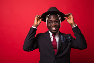 Portrait of young happy African businessman holding hat isolated on red background