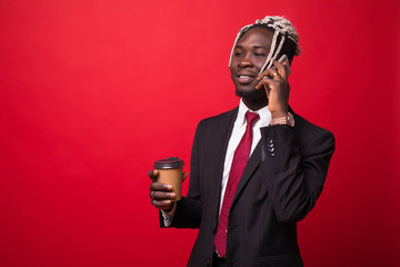 Thoughtful African businessman talking on mobile phone while holding coffee cup isolated against red background