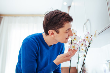 young man sniffing orchid at home