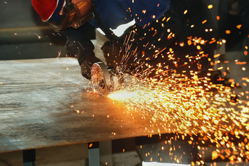 Worker in gloves and overalls cuts metal sheet angle grinder. Flying sparks from the disk....