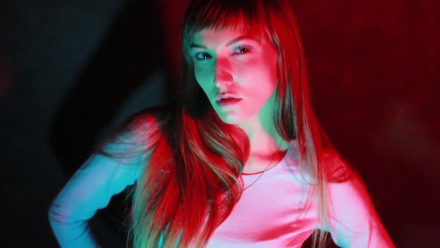 A beautiful young female face looks at the camera in a neon-red color, performs the image on the camera.