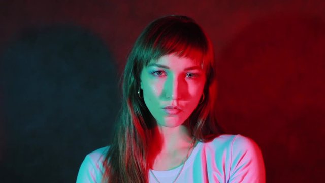 A beautiful young female face looks at the camera in a neon-red color, performs the image on the camera.
