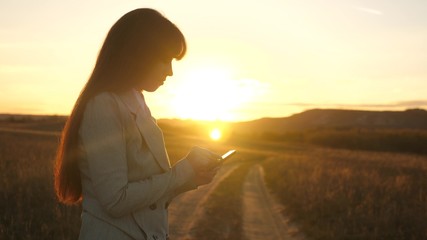 Female hands are holding a tablet and checking emails in the park at sunset. fingers of girl touch screen of tablet, smartphone. girl's hand prints a mobile message on the smartphone screen.
