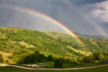 Fototapeta premium Beautiful mountain valley with green hills and huge rainbow