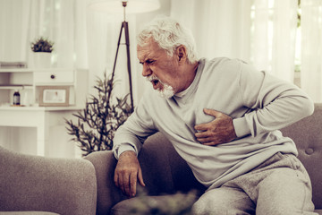 A grey-haired man experiencing terrible heartache while sitting at sofa