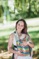 Informal mother carry baby girl in baby carrier in park