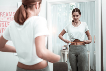 Teenager girl looking at her body parameters near the mirror