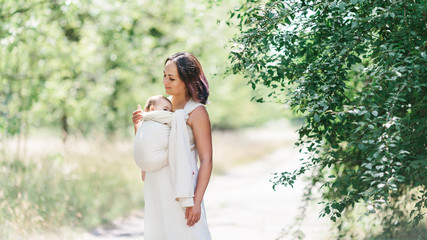 Mother carry baby girl in wrap sling in park.