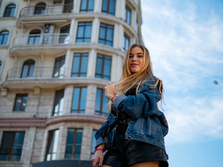 attractive girl with flowing hair in a denim jacket against the backdrop of a modern building and blue sky