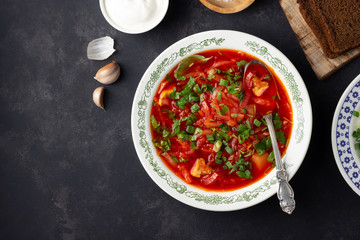 Ukrainian beet red soup - borscht with sour cream on black stone background. Top view.