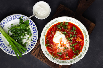 Ukrainian beet red soup - borscht with sour cream on black stone background. Top view.