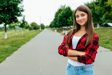 Fototapeta premium Happy girl teenager 13-16 years old schoolgirl, stands road. In summer in city after school. Holiday weekend city. Red shirt T-shirt and jeans. Free space for text. Emotions of joy, fun, lifestyle.