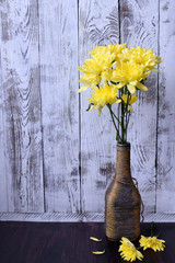 Bouquet of yellow chrysanthemum flowers in a vintage bottle against the white wooden background