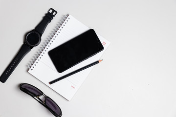 Top of notebook with pencil smart phone sunglasses on white table and flat lay