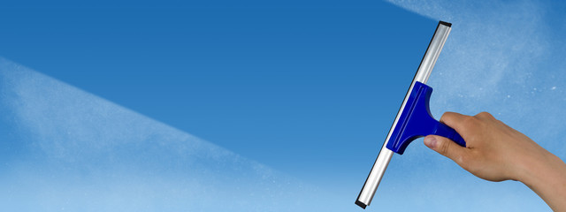 squeegee cleaning a dirty window, spring cleaning concept, blue sky with copy space