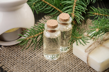 Obraz na płótnie Canvas Spruce essential oil in two bottles on linen napkin, natural soap, aroma lamp and fir branches around.