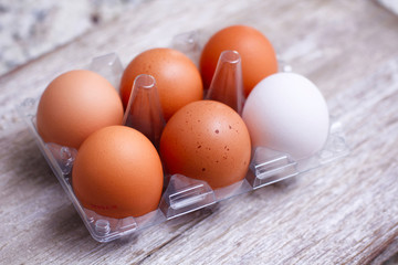 Set of eggs on clear plastic container on wooden table. Full pack. One different color egg. Brown and white. An exception. Egg carton box.
