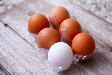 Set of eggs on clear plastic container on wooden table. Full pack. One different color egg. Brown and white. An exception. Egg carton box.