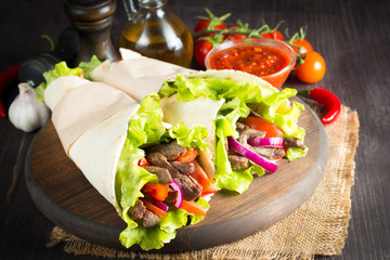 Photo of Mexican sandwich food, burrito, fajita, tacos, wrap made of tortilla, beef, chicken, fresh vegetables on rustic wooden background. Fast food concept. Healthy lunch snack. Copy space. 