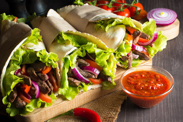 Photo of Mexican sandwich food, burrito, fajita, tacos, wrap made of tortilla, beef, chicken, fresh vegetables on rustic wooden background. Fast food concept. Healthy lunch snack. Copy space. 