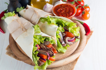 Photo of Mexican sandwich food, burrito, fajita, tacos, wrap made of tortilla, beef, chicken, fresh vegetables on rustic wooden background. Fast food concept. Healthy lunch snack. Copy space. 