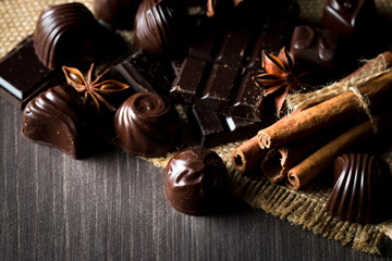 Assortment of dark, white and milk chocolate stack, chips. Chocolate and coffee beans on rustic wooden sacking background. Spices, cinnamon. Selective macro focus. Chocolates background. Sweets
