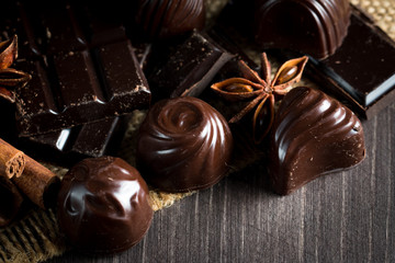 Assortment of dark, white and milk chocolate stack, chips. Chocolate and coffee beans on rustic wooden sacking background. Spices, cinnamon. Selective macro focus. Chocolates background. Sweets