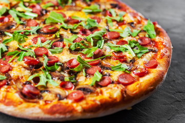Pizza with Mozzarella cheese, mushrooms, ham, tomato sauce, sausage, pepper, Spices and Fresh arugula. Italian pizza on Dark grey black slate background
