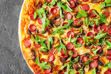 Pizza with Mozzarella cheese, mushrooms, ham, tomato sauce, sausage, pepper, Spices and Fresh arugula. Italian pizza on Dark grey black slate background