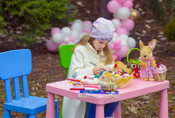 Cute, little girl coloring Easter eggs in the garden. Child activity and creativity. Easter concept