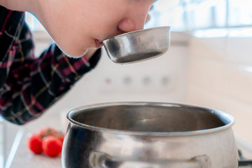 young man tasting the soup in the ladle while cooking at the kithcen  f
