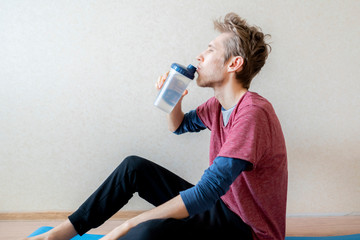 skinny young guy drinking water from shaker while sitting on the floor f