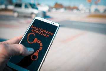 Hands using a smartphone with handcuffs and smartphone addiction words on screen. Internet addiction disorder, IAD, and Mobile phone overuse or smartphone addiction concept.
