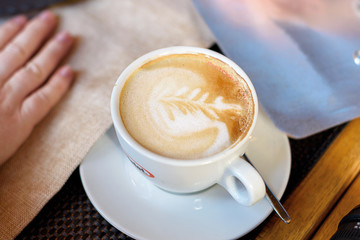 Cup of cappuccino with latte art. Beautiful foam, white cups. Hands in shot.