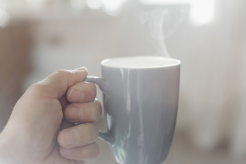 Man hand holding a cup of hot black coffee or americano with blurred natural background and morning sunlight
