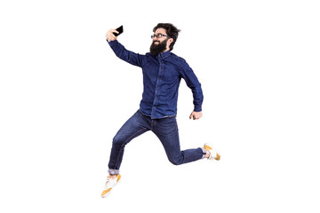 Full length portrait of a joyful bearded hipster man in glasses, jumping and taking selfie,...