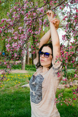 Brunette girl stands near a flowering tree. A warm Sunny day, blooming Apple tree.