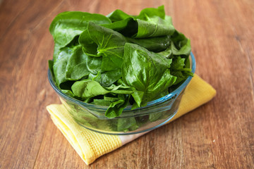 Fresh raw organic spinach leaves in a glass bowl on rustic wooden table