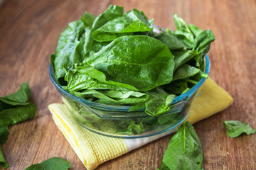 Fresh raw organic spinach leaves in a glass bowl on rustic wooden table