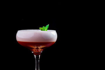 Elegant red ladies' cocktail with pink foam, decorated with mint, in a beautiful glass isolated on a black background. Close-up. Space