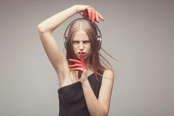 Fashion pretty girl listening music with headphones, wearing red gloves, take pleasure with song, and ask everybody to shut up, using her finger near mouth. Lifestyle woman concept