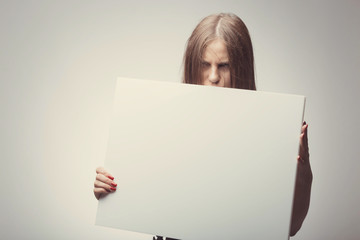 Fashion pretty girl holding white board with place for text. Angry girl looking on camera