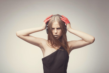 Fototapeta premium Fashion pretty girl listening music with headphones, wearing red gloves, and disappointed with bad music. Lifestyle woman concept