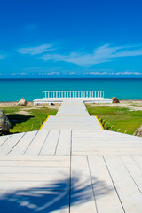 White wooden walkway on a tropical beach, with bright blue sky
