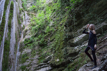 Fototapeta premium Young woman stands on the rocks near waterfall