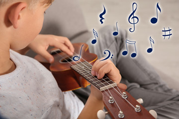 Little boy playing guitar on sofa in room, closeup