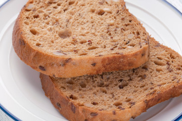 Slices of grain bread with mold. On a white plate with a blue stripe. On a wooden table